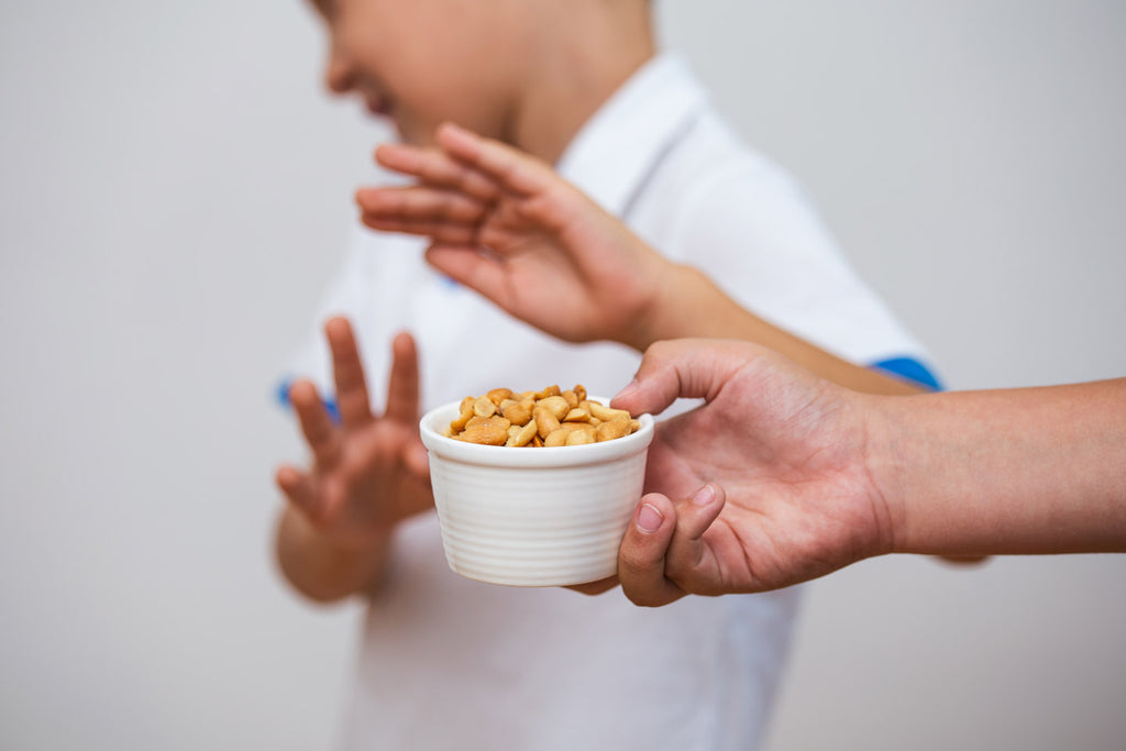 Child with autism and food allergies pushes bowl of peanuts away.