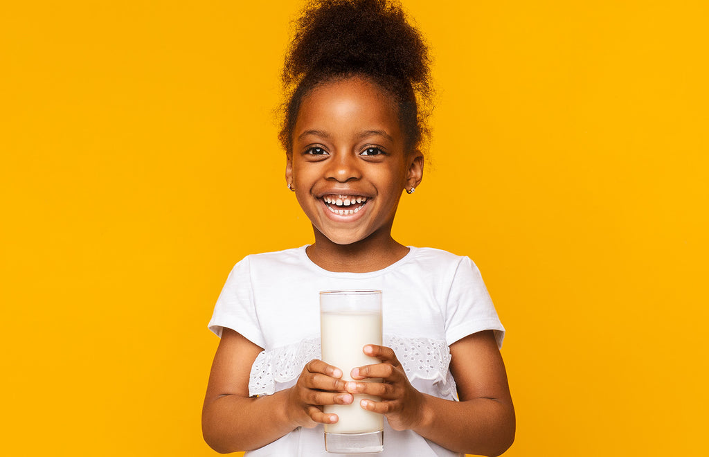 Young girl with Autism smiling while drinking a glass of milk in front of an orange background.